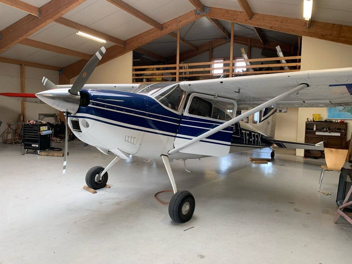 A white and blue Cessna 180 aircraft, registration TF-FFK, parked inside a hangar.