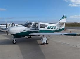 A white and green Commander 114B aircraft is parked on the tarmac.
