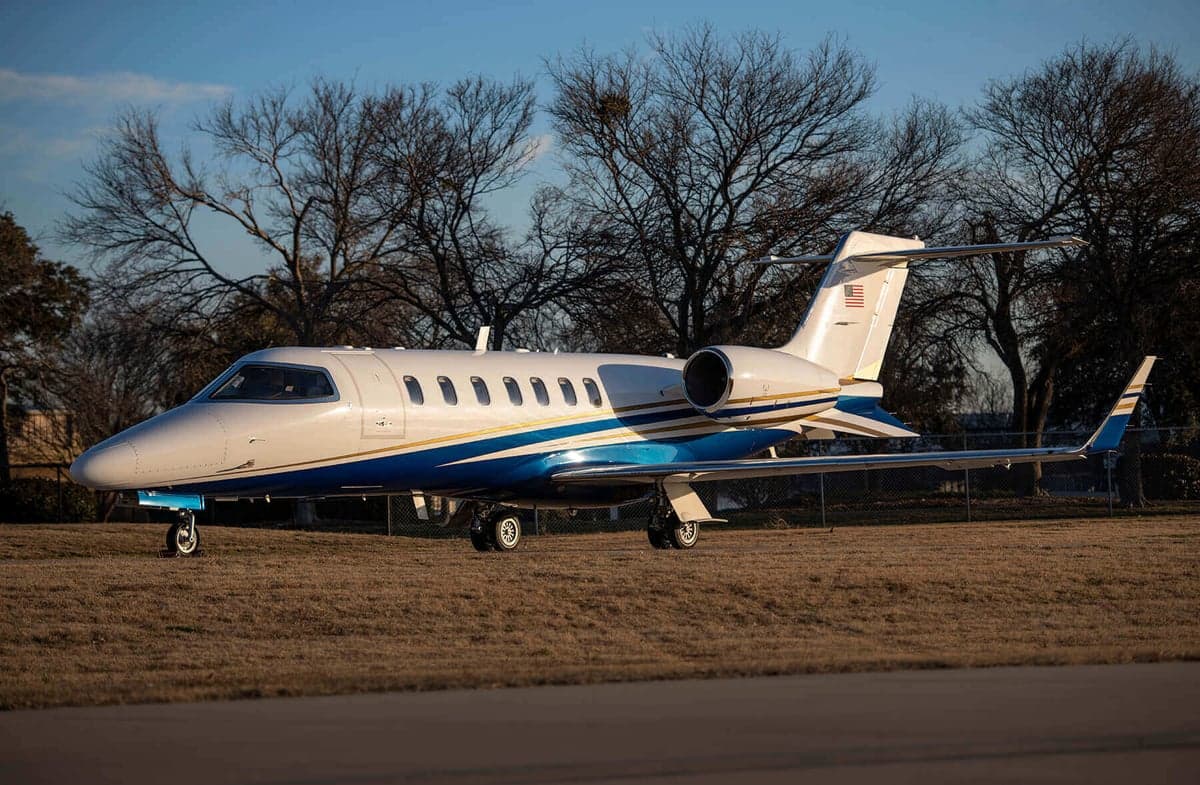 A Learjet aircraft is parked on the ground with a blue and gold stripe.