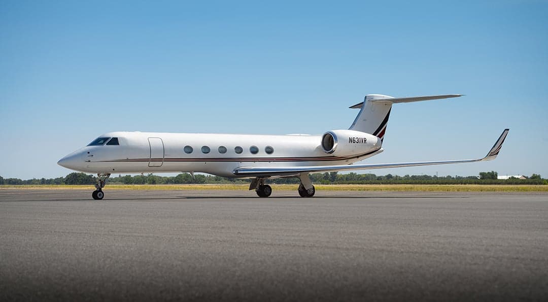 A white Gulfstream G550 business jet with a red and black stripe on the tail, registration N631VR, parked on an airfield.