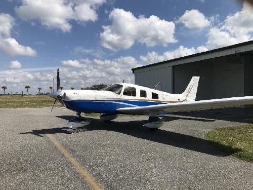 A Piper PA-28-181 Archer II aircraft with a blue and white paint scheme parked on the tarmac.