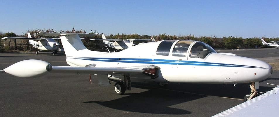 A white BD-5 aircraft with blue stripes is parked on the tarmac.