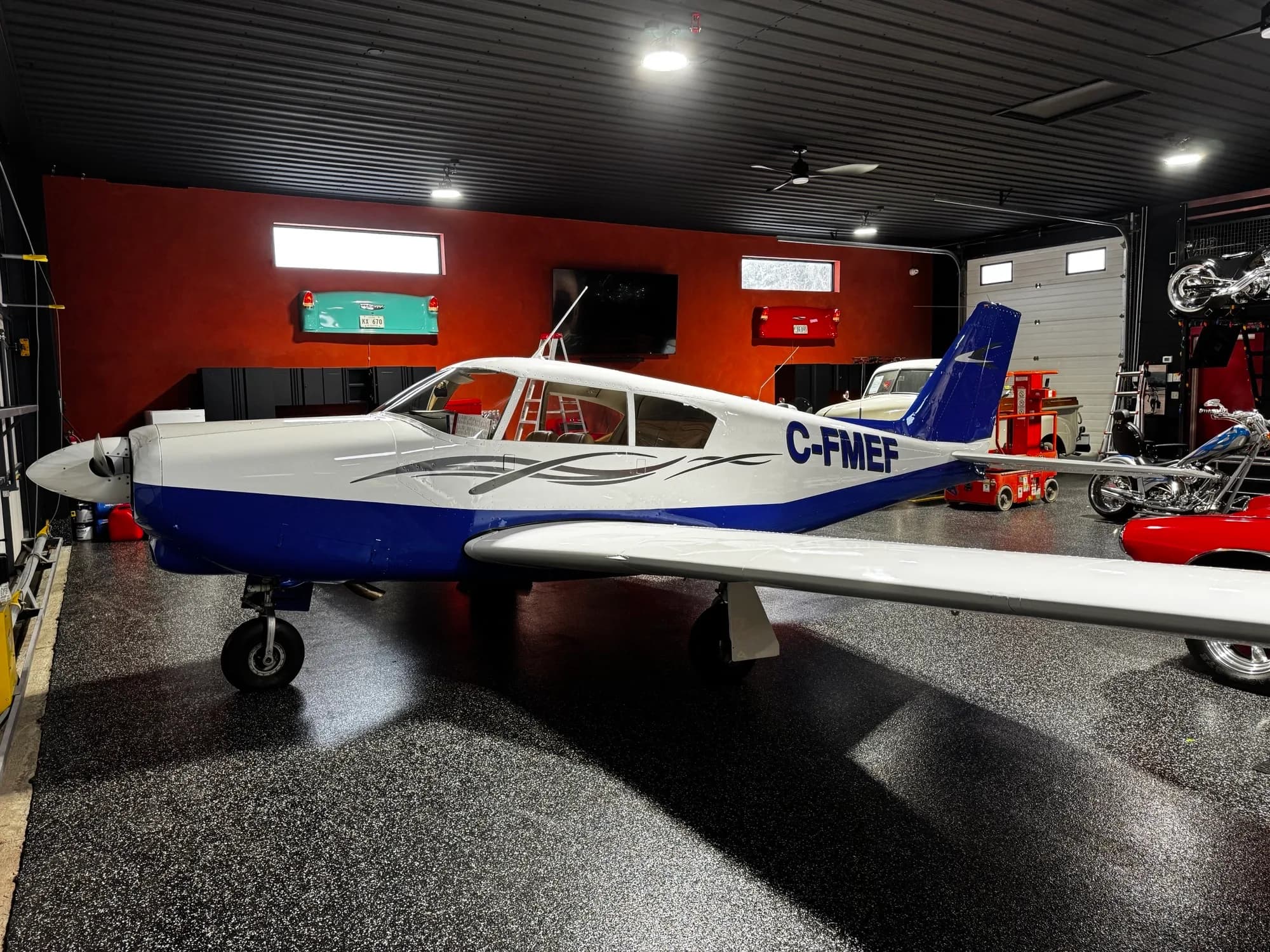 A white and blue single-engine propeller aircraft, registration C-FMEF, parked in a well-lit garage.