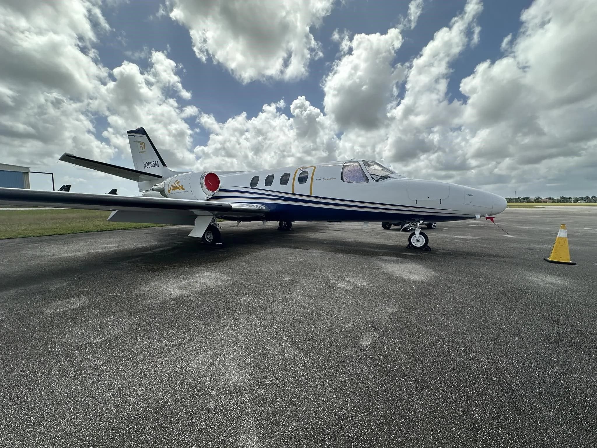 A white and blue Cessna Citation jet (N3095M) parked on an asphalt ramp under a cloudy sky.