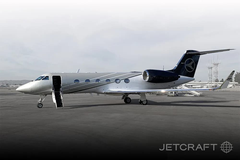 A silver and dark blue Gulfstream G450 business jet with its main door open and stairs deployed, parked on a tarmac.
