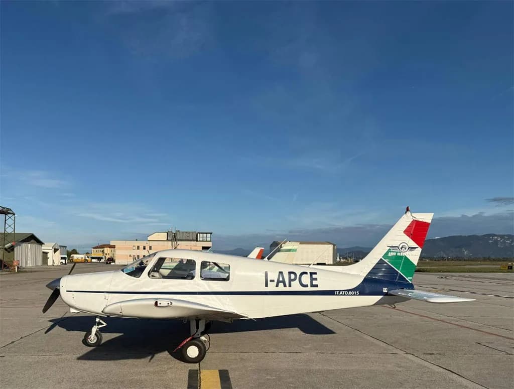 A white single-engine propeller aircraft with "I-APCE" registration and "Aero Club Brescia" logo on the tail, parked on an airfield under a blue sky.