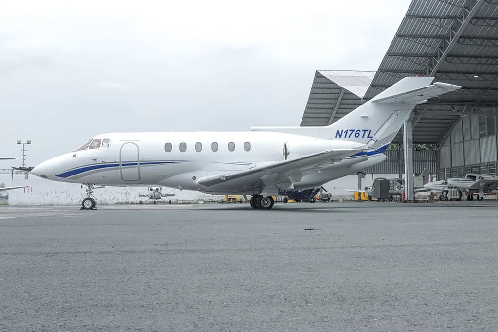 A white business jet with blue and grey stripes, registration N176TL, parked on an tarmac next to a hangar.