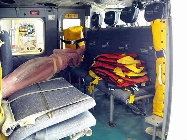 The interior cabin of a helicopter showing passenger seats, stacked life vests, and equipment.