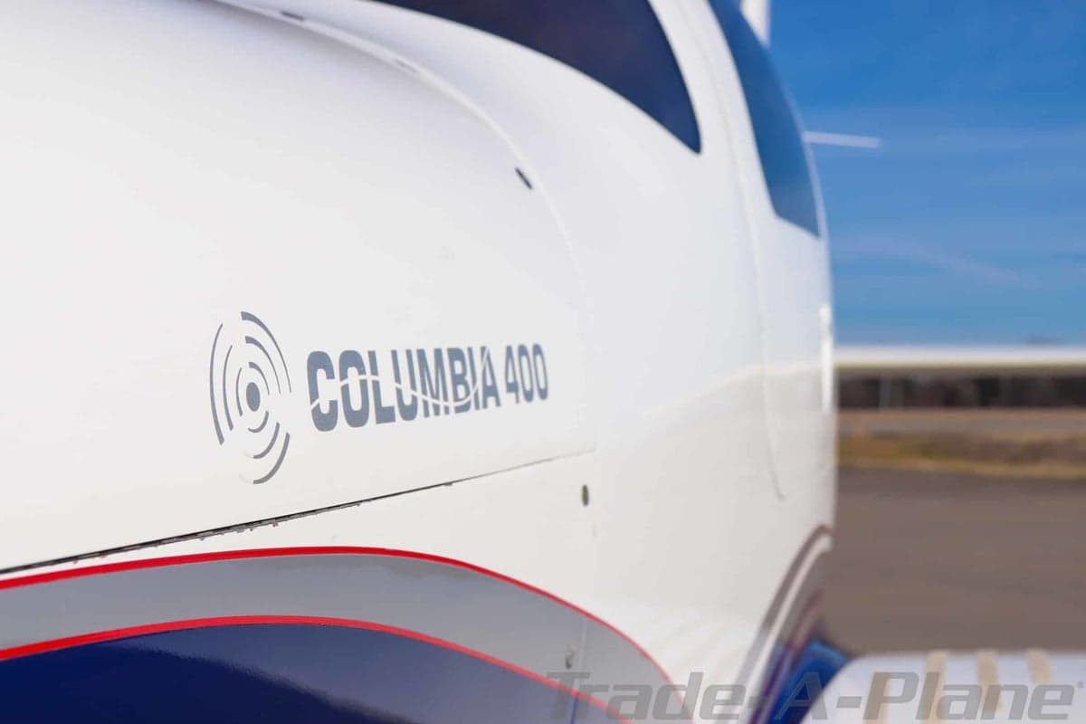 Close-up of the white and blue fuselage of a Columbia 400 aircraft on an airfield.