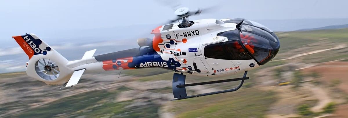 Airbus H130 helicopter in flight with a unique paint scheme.