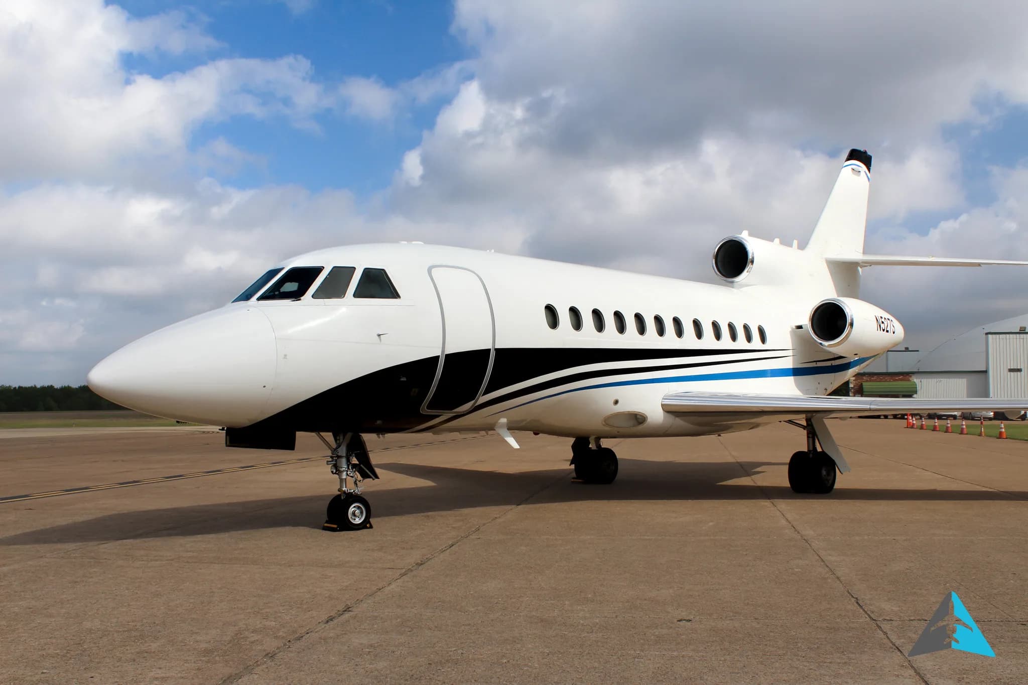 A white Dassault Falcon 900EX business jet with black and blue stripes parked on an airfield.