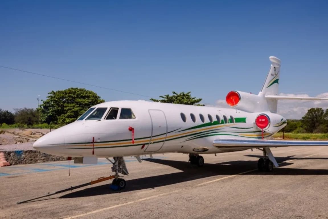 A Dassault Falcon 900EX aircraft with green and gold stripes on the tarmac under a clear sky.