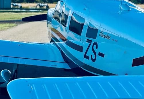 A Piper Cherokee SIX 260 aircraft with ZS- registration, showing its white and dark stripe paint scheme on an airfield.