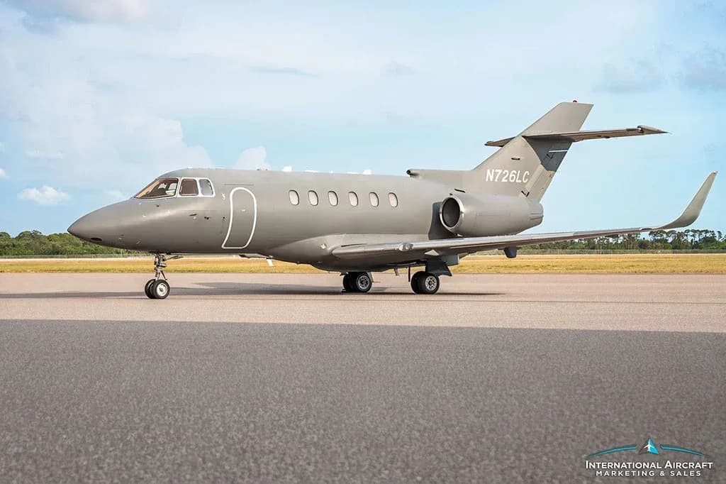 A gray business jet, N726LC, is parked on an asphalt runway under a partly cloudy sky.