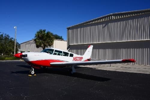 A white and red painted aircraft, N9338P, is parked on the tarmac in front of a hangar.