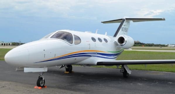Cessna Citation Mustang on the tarmac with blue and green stripes.