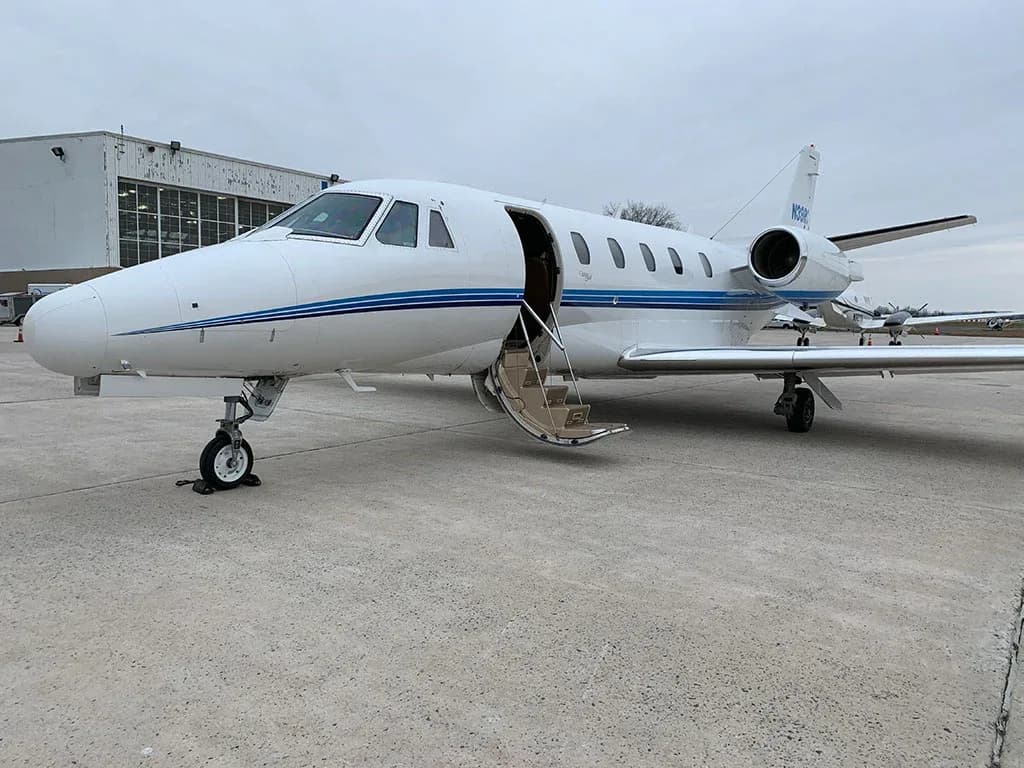 A white business jet with blue stripes and registration N39RC parked on an airfield with its main door open.