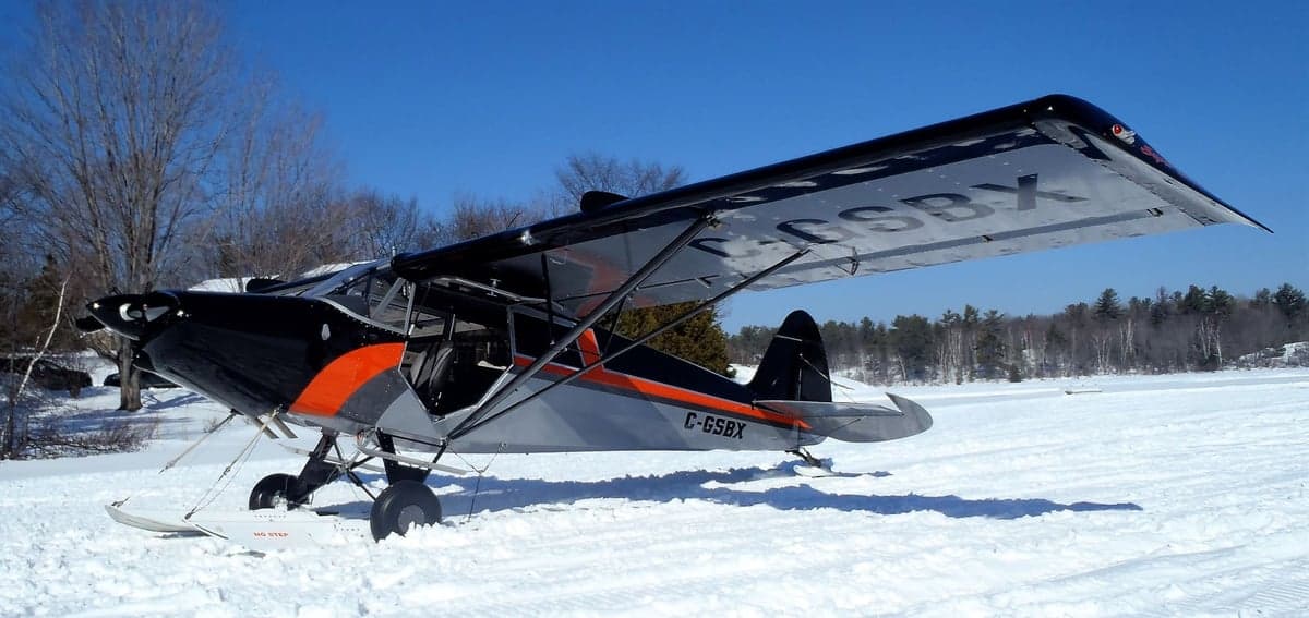 A black, gray, and orange Super Cub on skis is parked on a snowy surface.