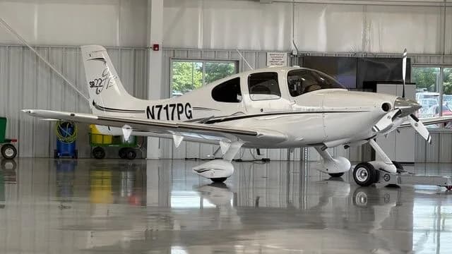 White Cirrus SR22T aircraft N717PG with black and grey stripes parked inside a hangar.