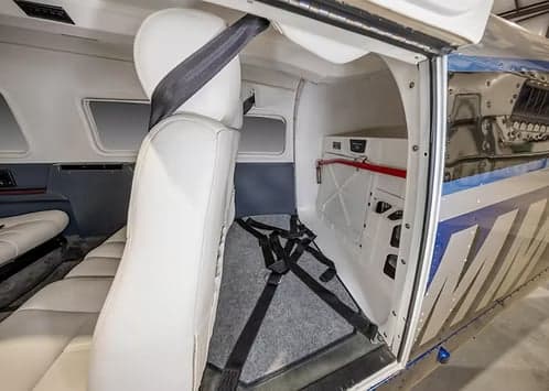 The aircraft's interior cabin with white seats and a view into the rear baggage compartment.