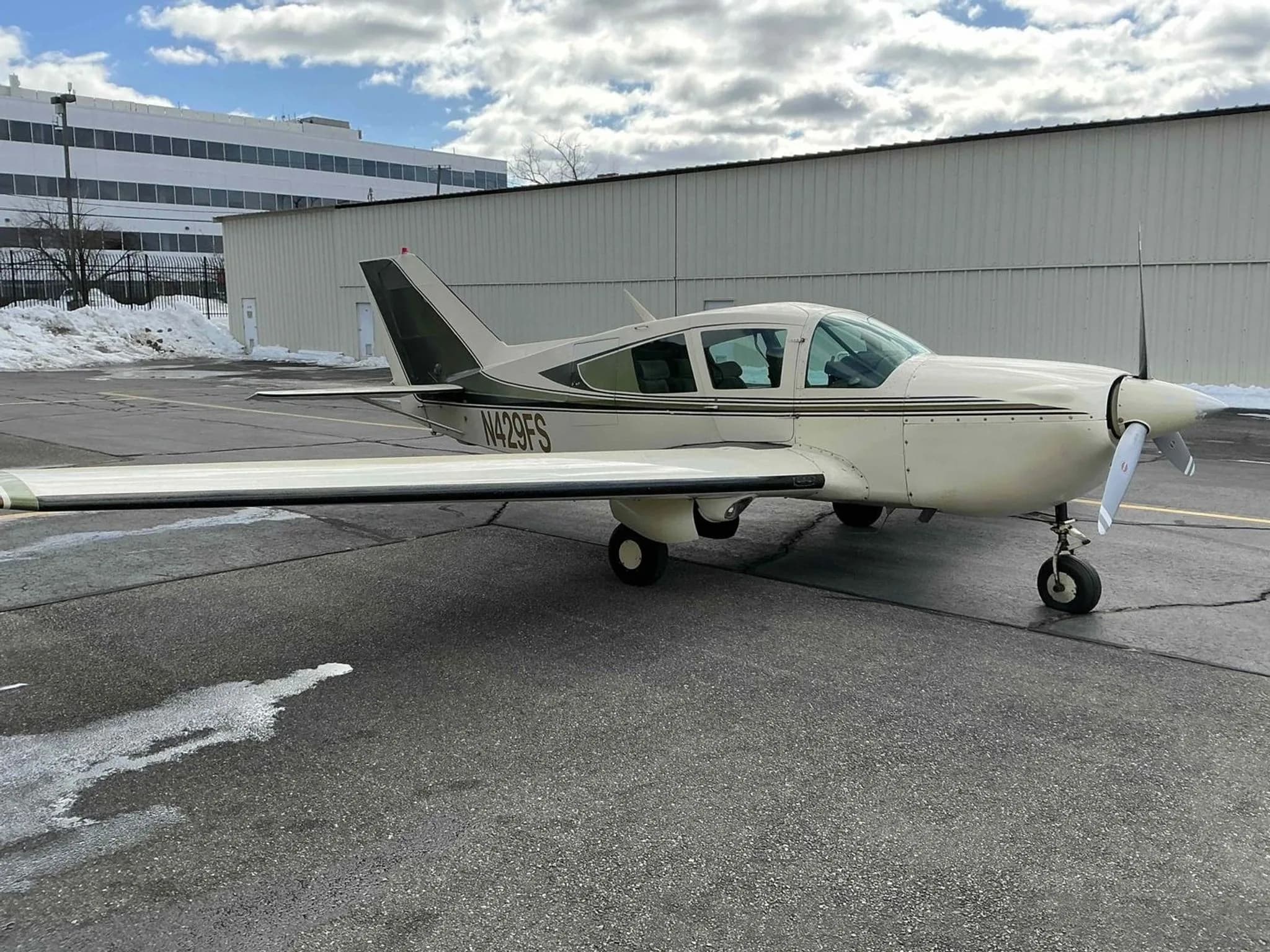 A white and green Bellanca Viking aircraft, N429FS, parked on an asphalt ramp with snow and a building in the background.
