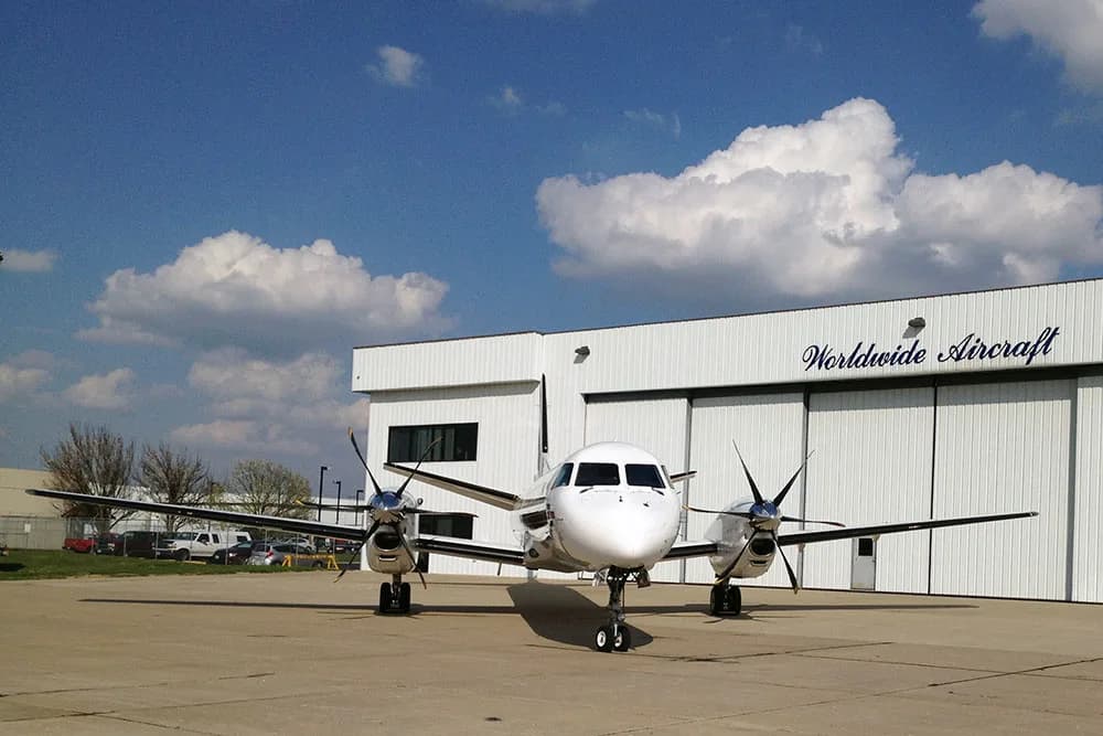Front view of a white aircraft parked in front of a hangar.