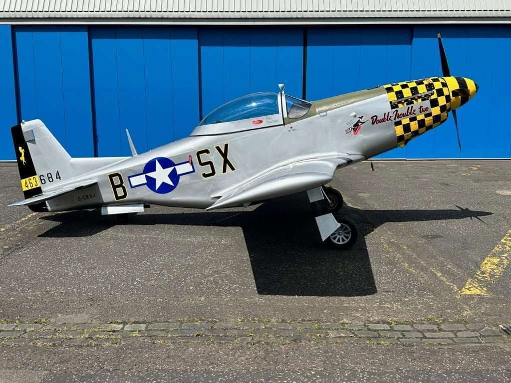 A P-51 Mustang with a checkerboard nose sits on the tarmac.
