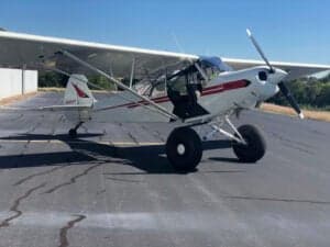 A white and red Piper Cub sits on the tarmac.