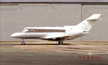 Side view of a white business jet with a dark brown stripe, parked on a tarmac in front of a hangar.