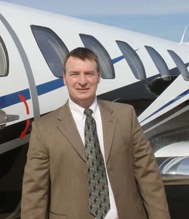 A man in a suit stands in front of a white business jet with blue stripes.