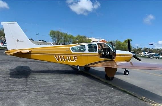A yellow and white single-engine aircraft, registration VH-HLP, with its door open, parked on an asphalt apron under a blue sky.