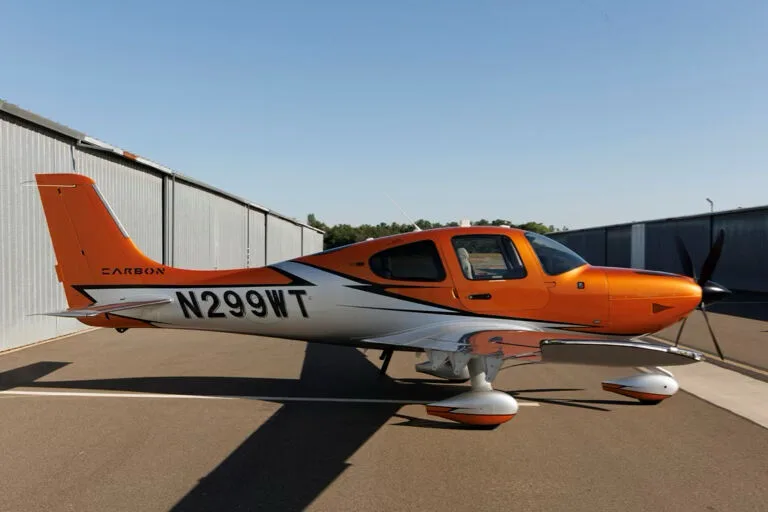 Side view of an orange and silver Cirrus SR22T GTS aircraft with registration N299WT parked on an tarmac.