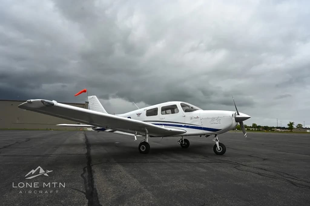 A white single-engine propeller aircraft with blue accents parked on an asphalt tarmac under a cloudy sky.
