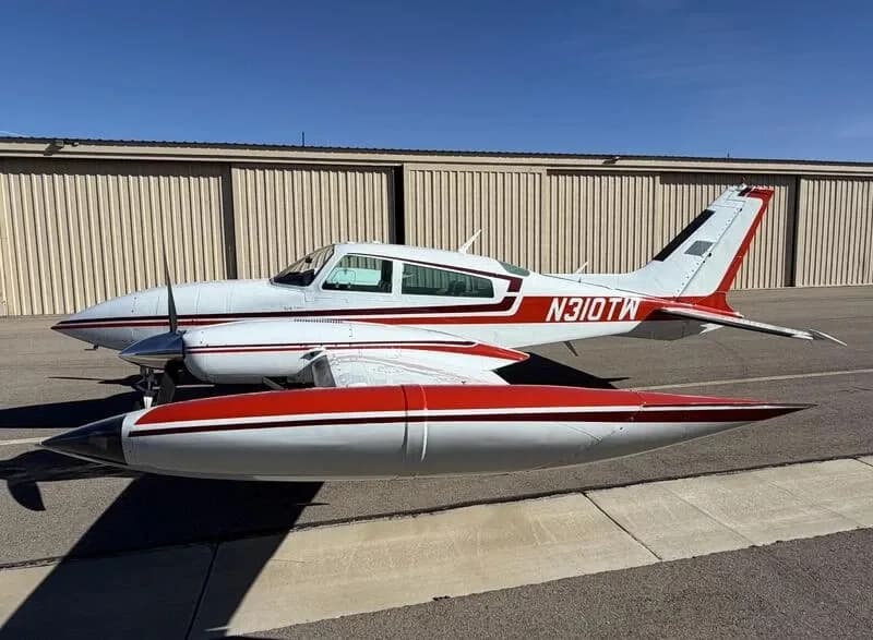 Side view of a white and red Cessna 310 twin-engine aircraft with tip tanks on an airfield.