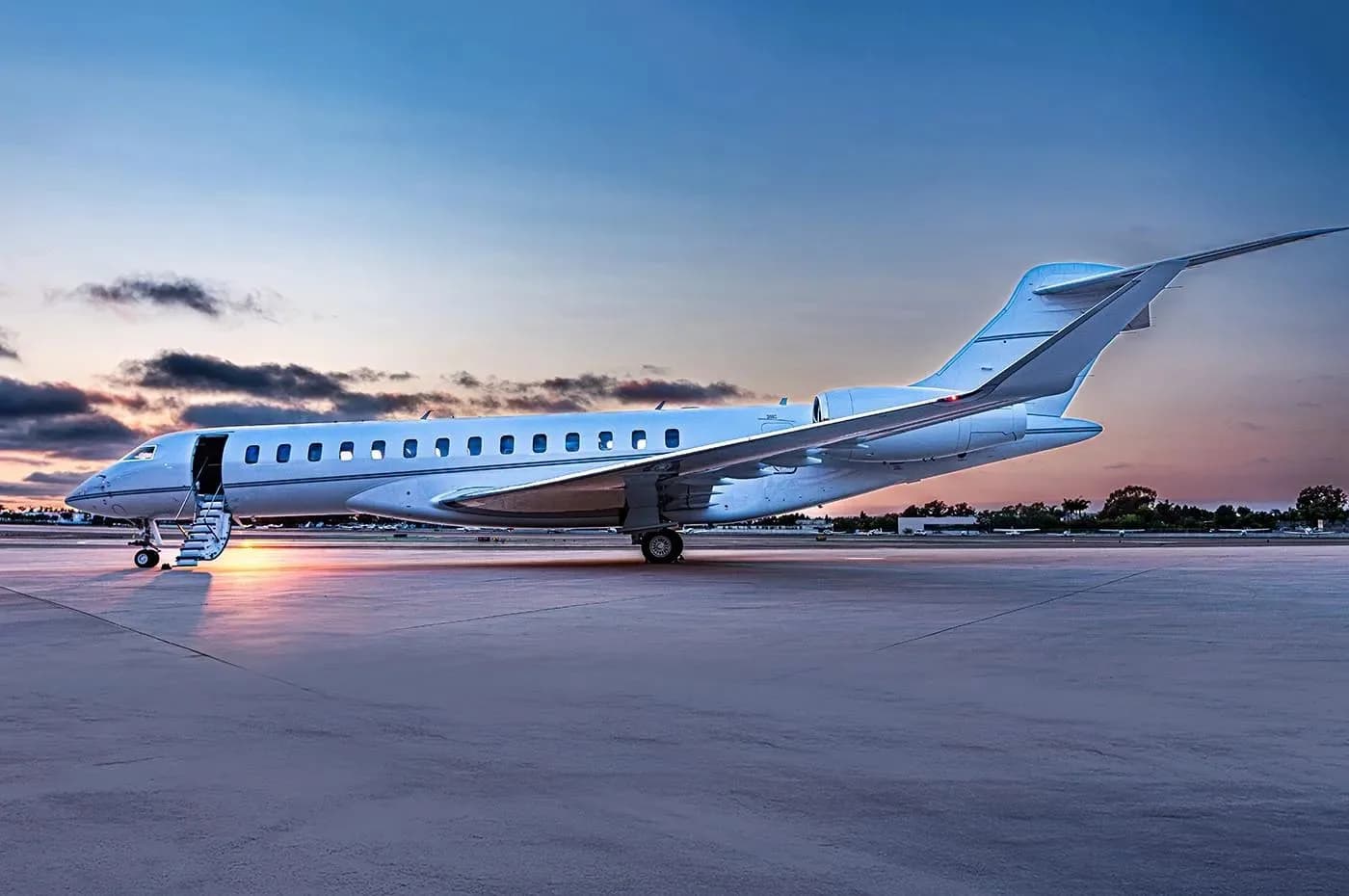 A white business jet with its door open and stairs extended, parked on a tarmac at sunset.