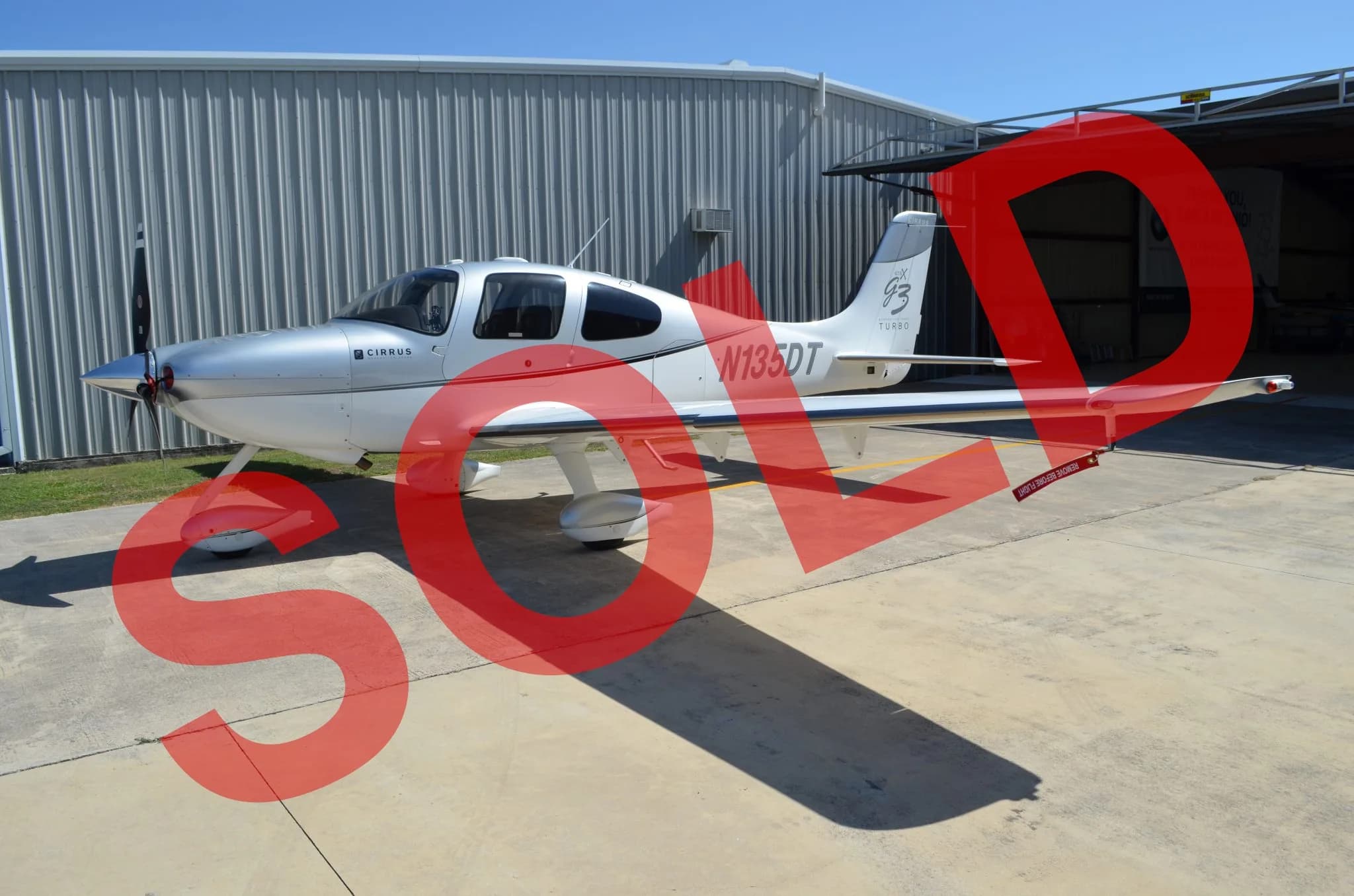 A silver and white Cirrus SR22T Turbo aircraft with registration N135DT is parked on an apron outside a hangar.
