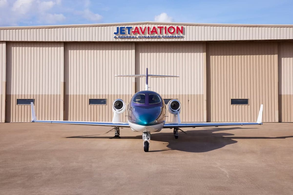 Front view of a HondaJet parked in front of a Jet Aviation hangar.