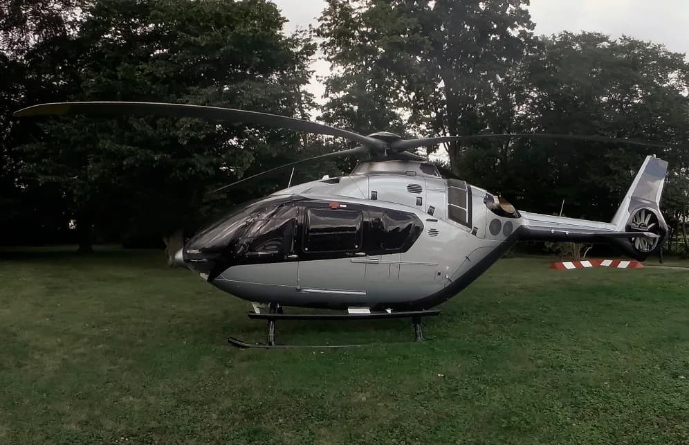 Side view of a silver and black helicopter parked on the grass.