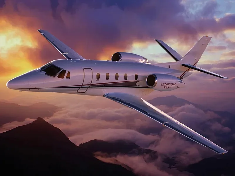 A Citation XLS+ flying over a mountainous landscape at sunset.