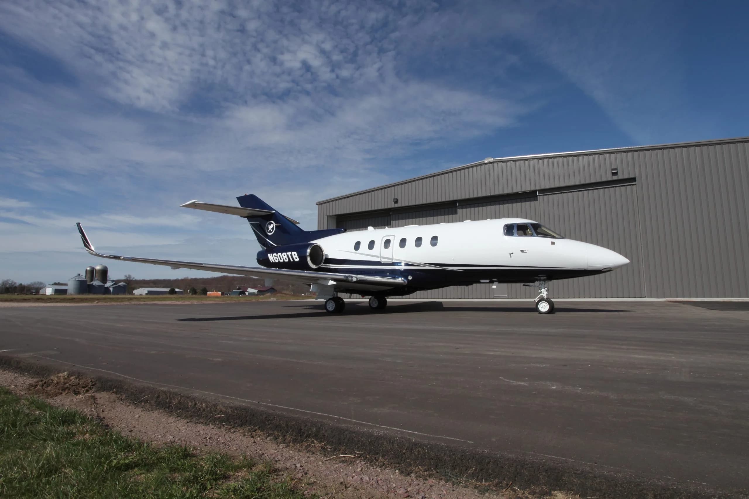 A Hawker 400XP aircraft is parked on the tarmac in front of a hangar on a sunny day.