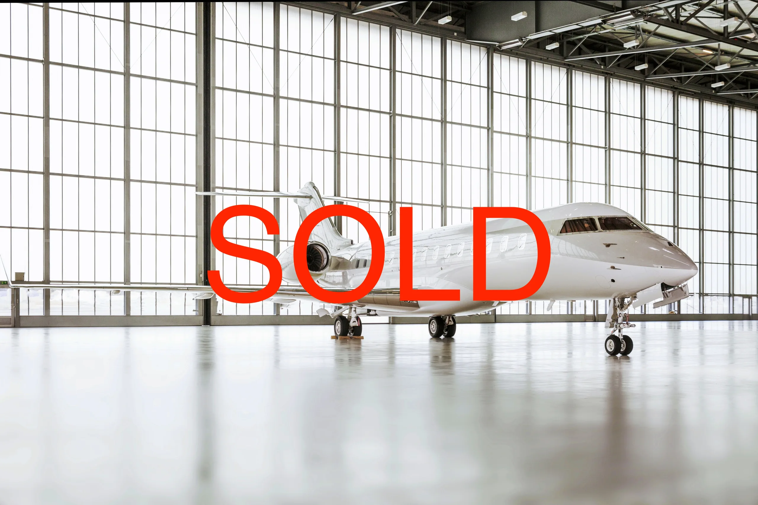 A white business jet with a light grey nose cone parked inside a modern hangar.