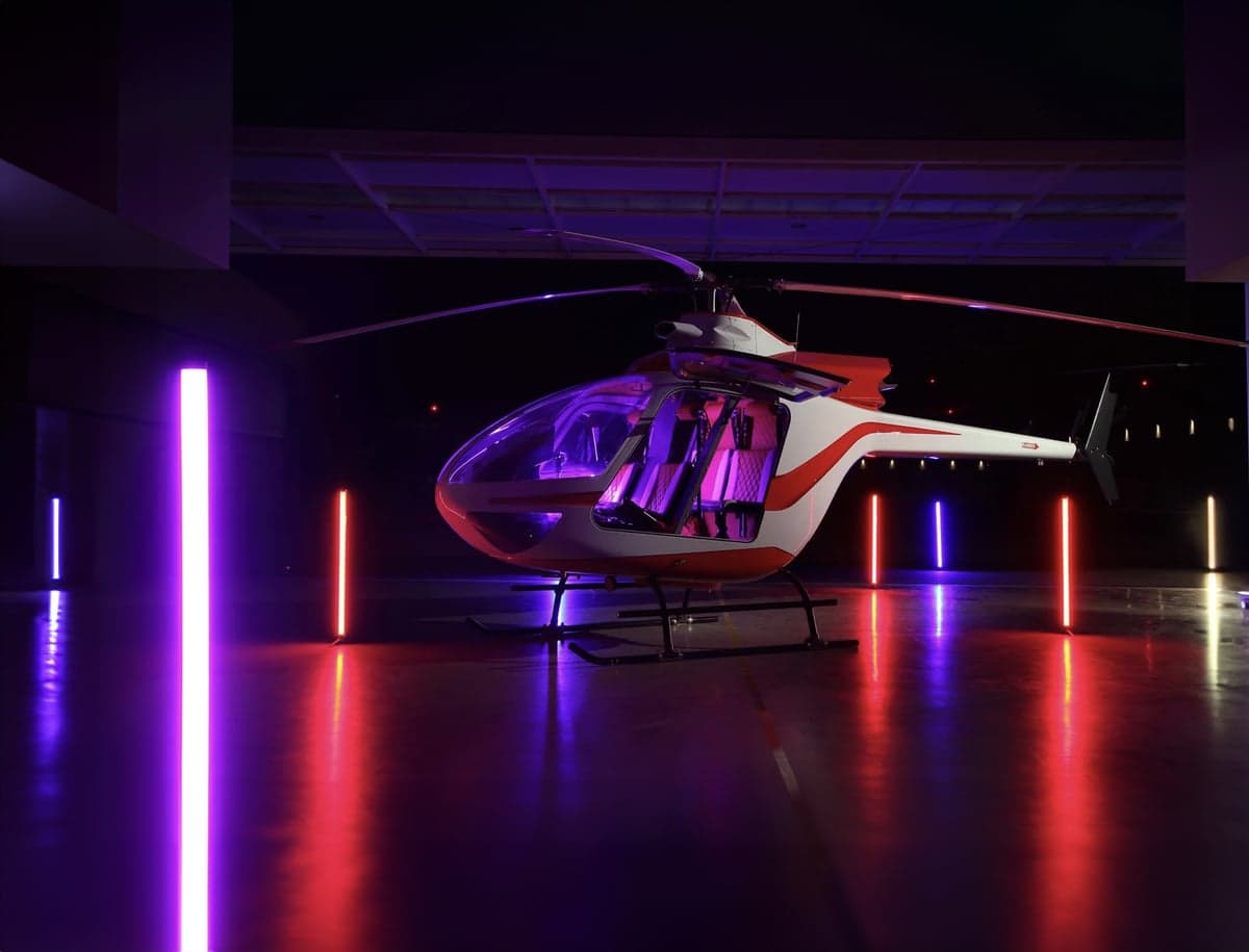 A white and red helicopter is parked in a hangar with colorful lights.