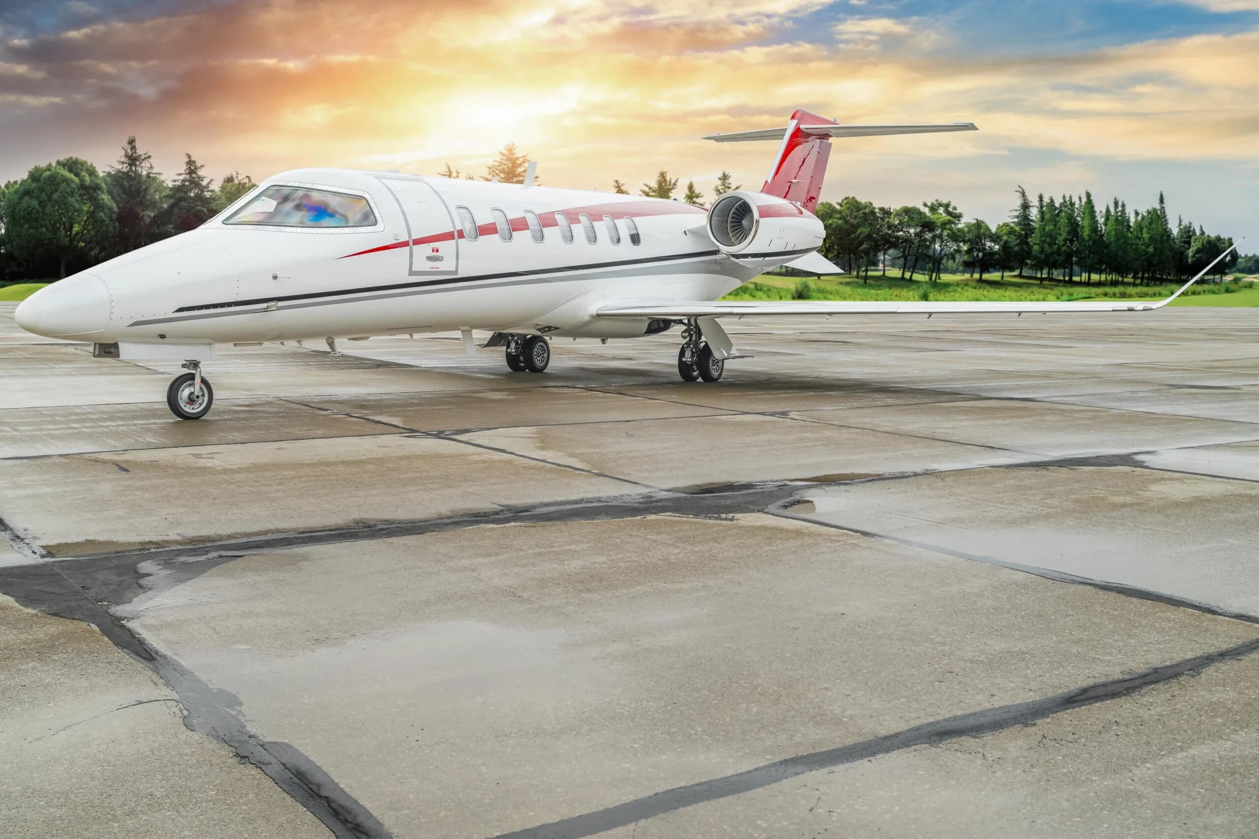 A Learjet aircraft is parked on the tarmac with a red and white paint scheme under a colorful sky.
