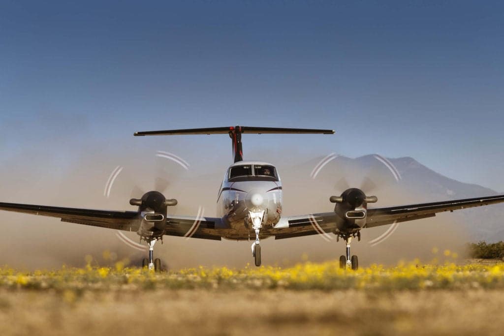 Front view of a King Air 350 on a grassy field with mountains in the background.
