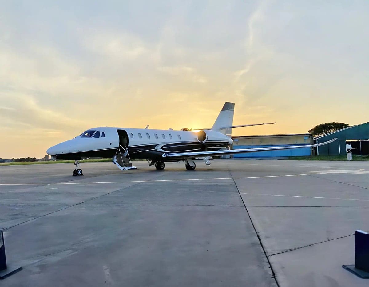 A Citation CJ4 aircraft is parked on the tarmac with the door open at sunset.