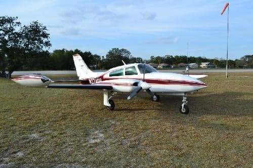 A white and maroon Beechcraft Baron is parked on a grassy field.