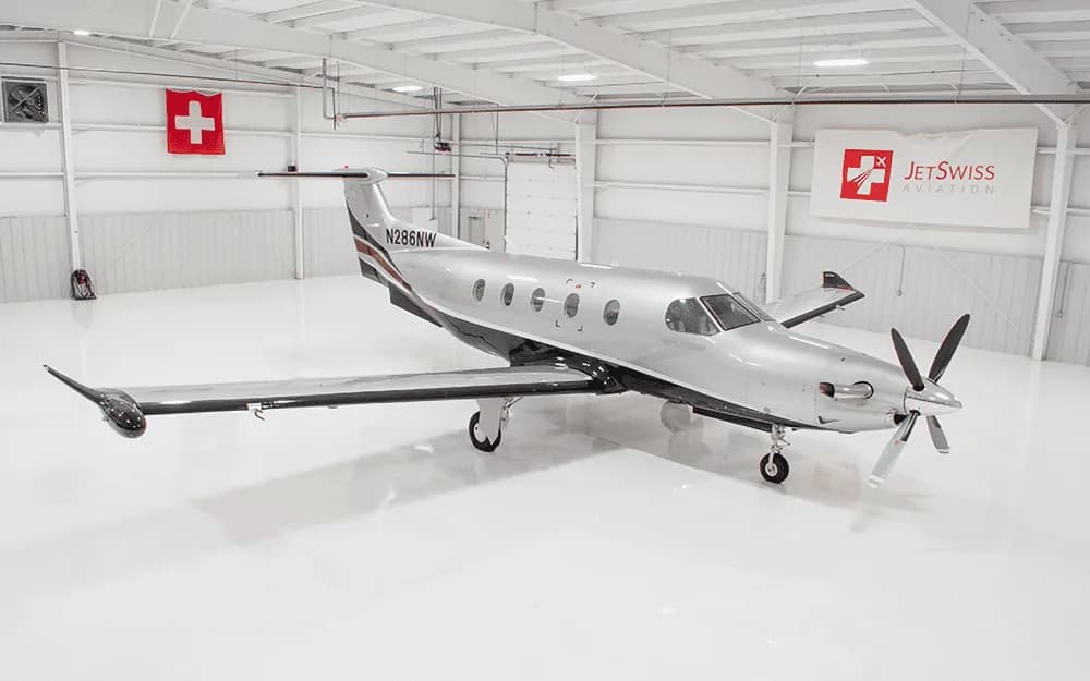 A silver and black Pilatus PC-12 NG aircraft with registration N286NW parked in a brightly lit hangar.