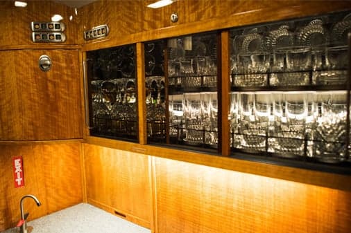 A luxurious aircraft galley with polished wood cabinetry and shelves filled with glassware.