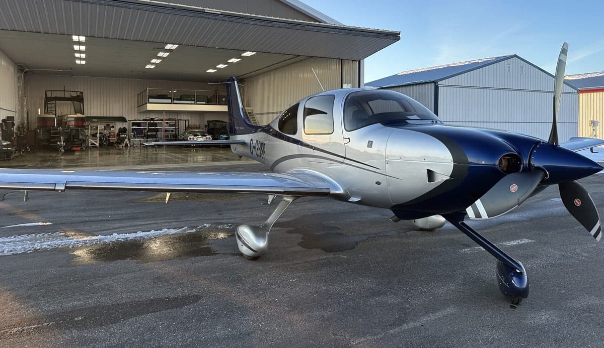 A Cirrus aircraft is parked outside a hangar on a sunny day.