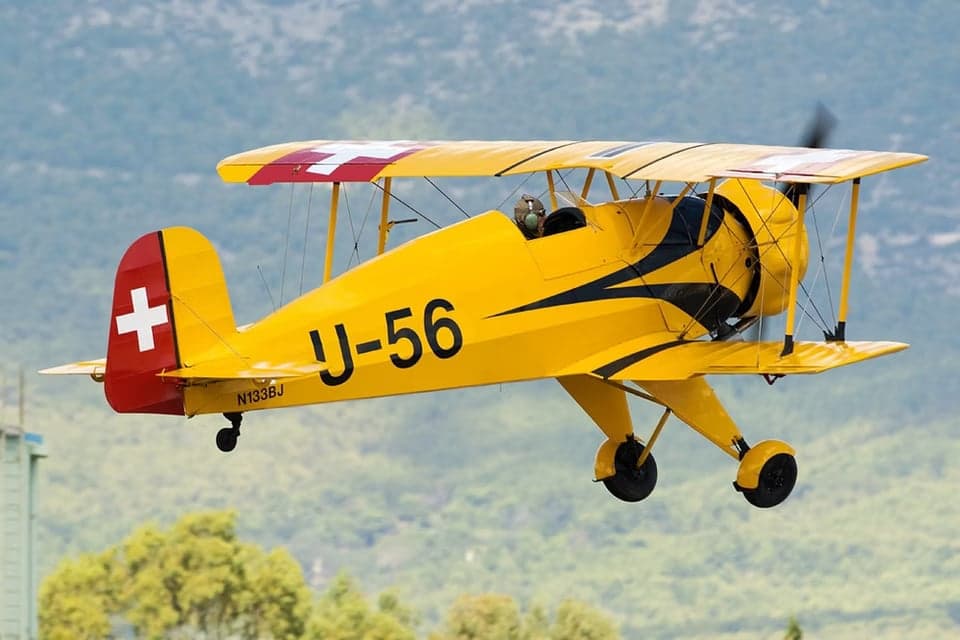 A yellow biplane with Swiss markings in flight.
